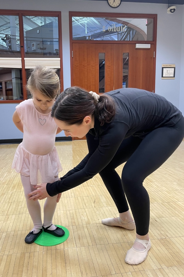 An instructor teaching a young girl in pink dress how to pose